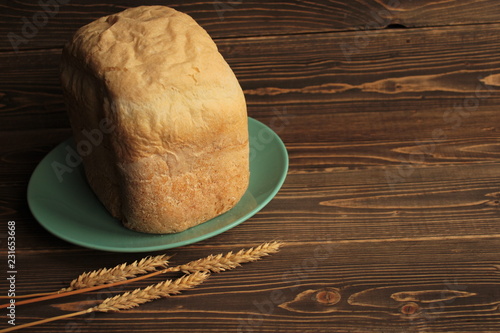 Хлеб на голубом блюде, и колоски пшеницы на деревянном столе. 