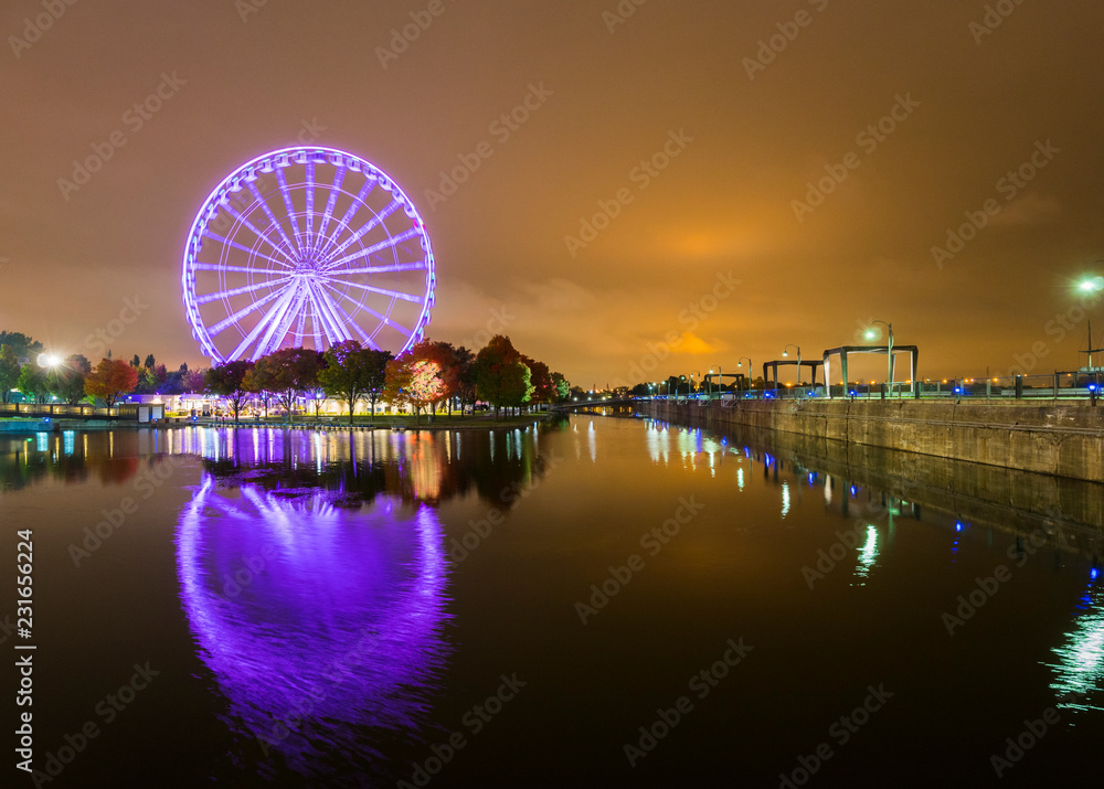 A brightly lit ferris wheel in the old port area of Montreal, Canada. Beautifully reflected in the water