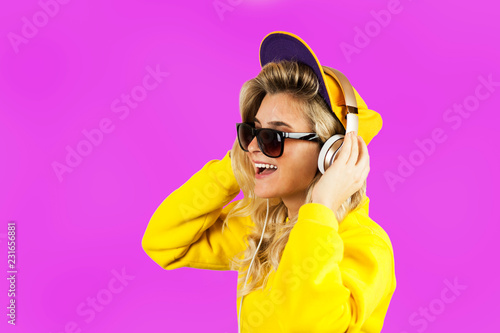 Pretty young emotional girl in earphones listening to music isolated on purple background