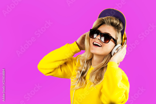 Pretty young emotional girl in earphones listening to music isolated on purple background