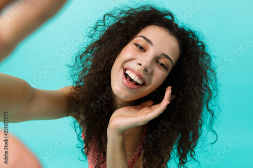 Image of cheerful woman 20s wearing casual clothing laughing while taking selfie photo, standing isolated over blue background