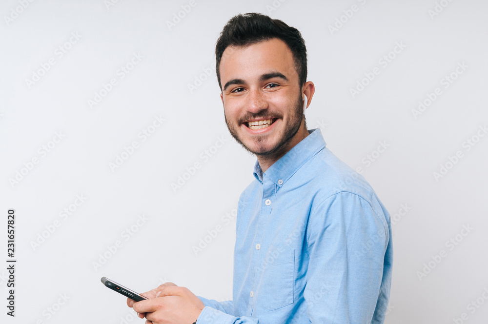 Smiling young man in causal holding phone and listening music at airpods Smiling young man in causal holding phone and listening music at airpods