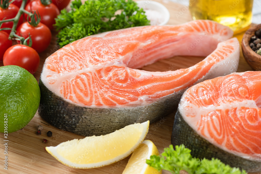 Fresh salmon steaks and ingredients for cooking, lemon lime olive oil spices cherry tomatoes and green salad leaf Fresh salmon steaks and ingredients for cooking, lemon lime olive oil spices cherry tomatoes and green salad leaf