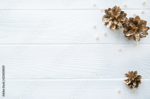 Heap of golden pine cones (painted fir cones) and placer of beige beads on white rustic background, top view, copy space. Christmas background for greeting. 
