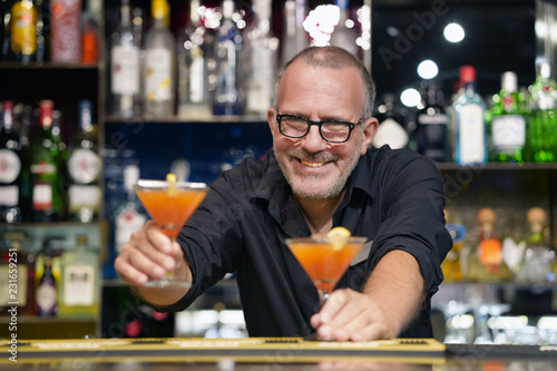 The barman gives a cocktail to the client of the hotel bar. Fresh cocktail. Alcoholic, non-alcoholic drink-beverage at the bar counter in the night club. Glass of grapefruit cocktail.