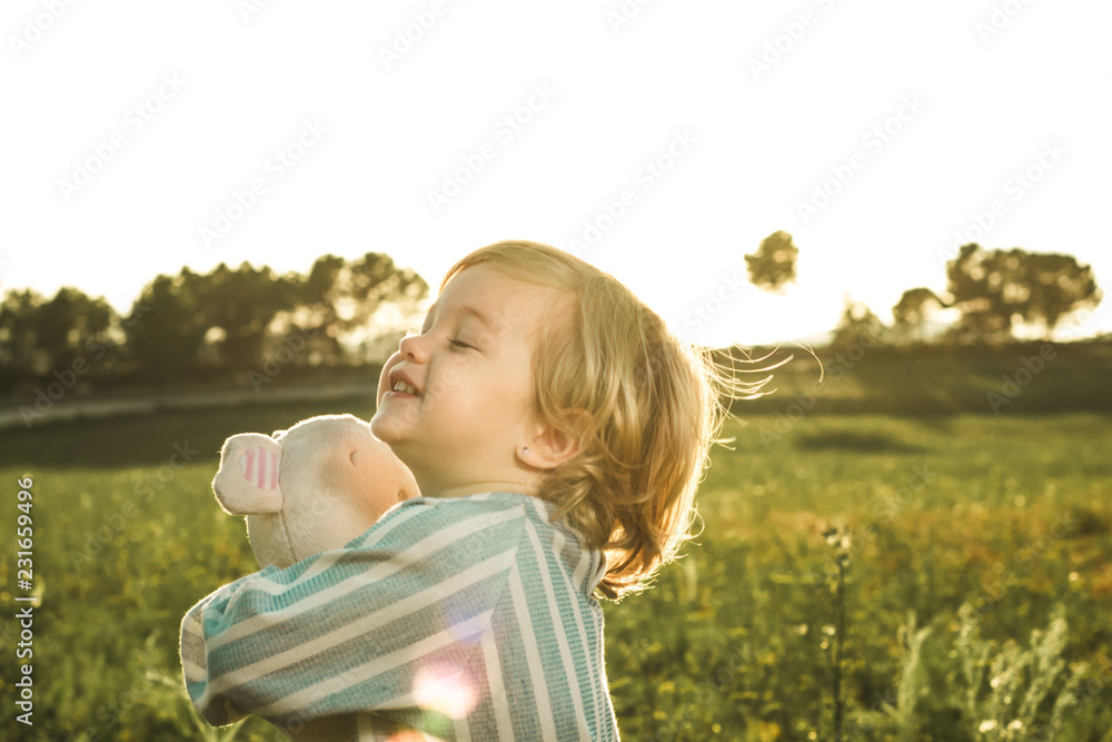 Happy little girl playing with a stuffed animal on the field Happy little girl playing with a stuffed animal on the field