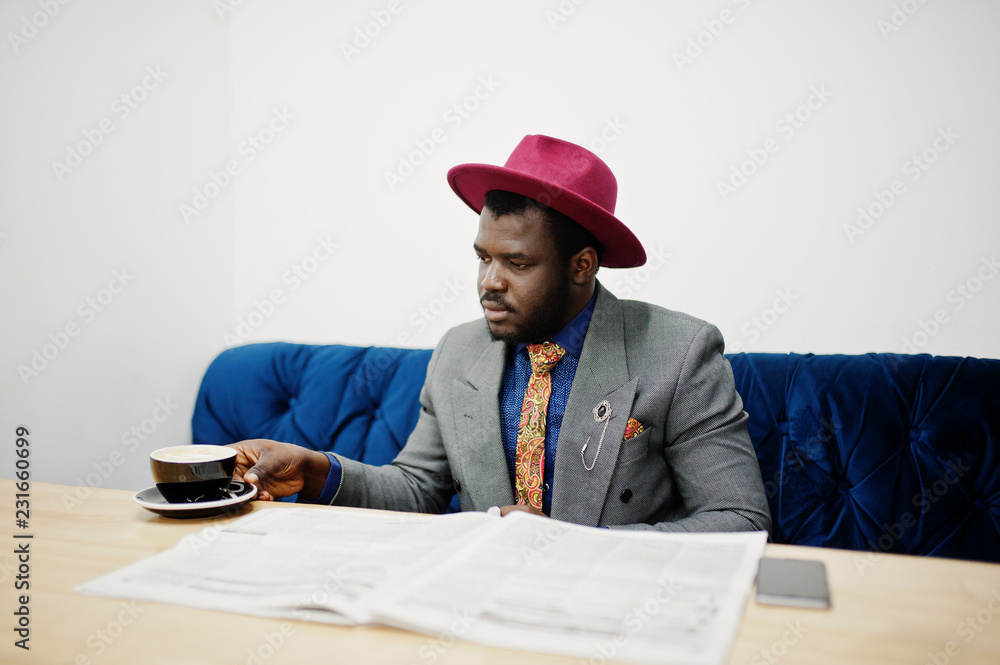 Stylish African American man model in gray jacket tie and red hat drink coffee at cafe and read newspapers. Stylish African American man model in gray jacket tie and red hat drink coffee at cafe and read newspapers.