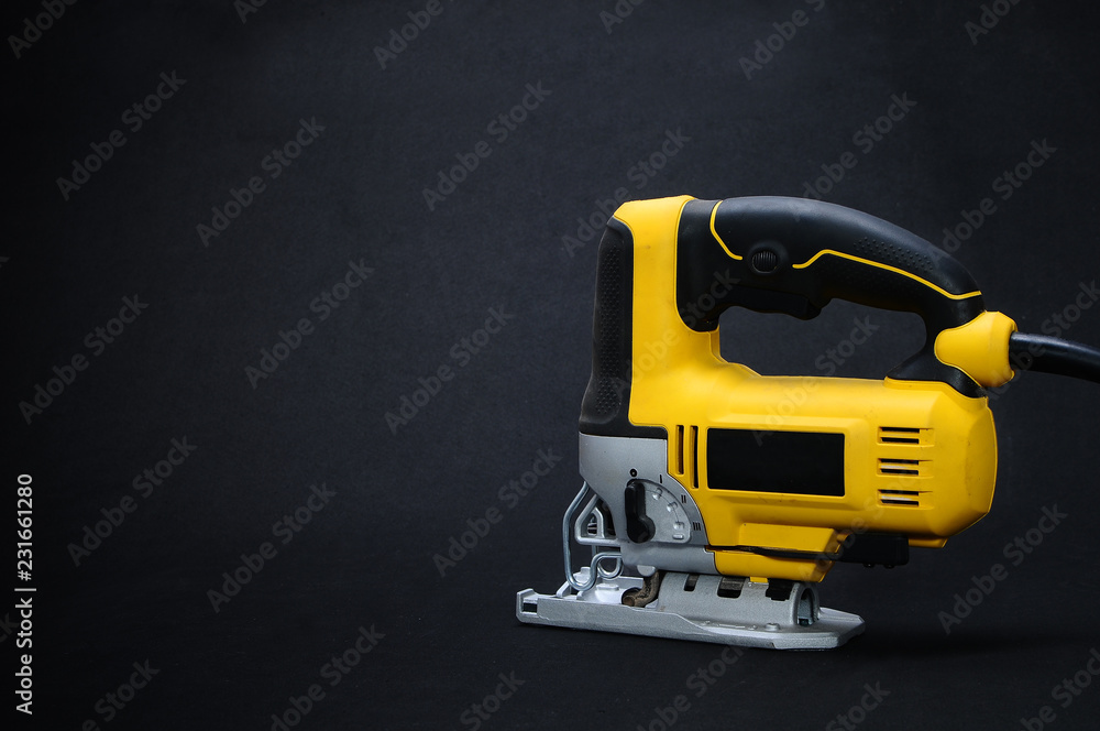 Isolated back side yellow electric jig saw on a dark background