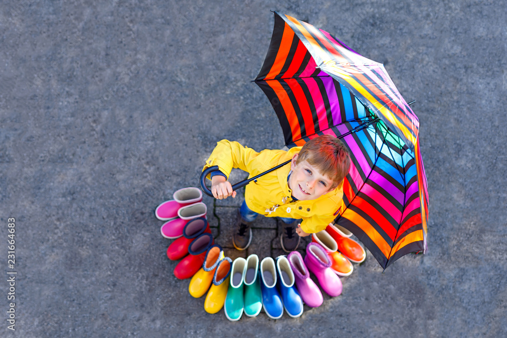 Little kid boy and group of colorful rain boots. Blond child