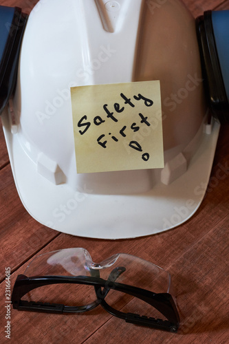 Safety first note one yellow piece of paper stuck on wooden background with full set of personal protective equipment: helmet, safet glasses and ear protection. photo