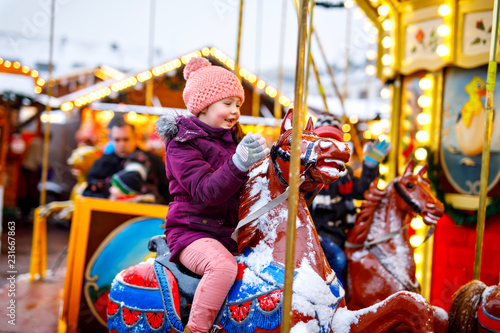 Adorable little kid girl riding on a carousel horse at Christmas funfair or market, outdoors.