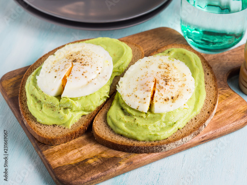 Rye bread avocado toasts with poached egg on wooden serving board. Brunch lunch meal