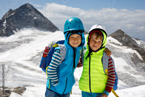 Two little boys with safety helmets and clothing with mountains landscape backgrounds. Kids hiking and discovering glacier in Tirol, Austria, Hintertux