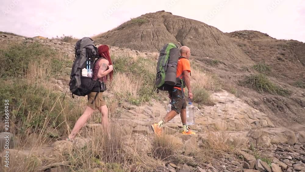 Tourists in full gear go hiking on a mountain road. Slow motion Tourists in full gear go hiking on a mountain road. Slow motion