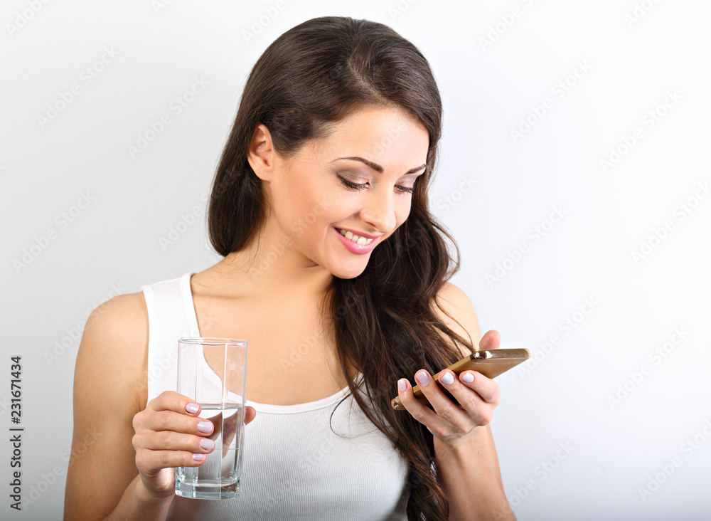 Happy smiling young woman with healthy skin reading and writing in mobile phone sms and drinking clean water. Consulting the diet. Closeup portrait. Happy smiling young woman with healthy skin reading and writing in mobile phone sms and drinking clean water. Consulting the diet. Closeup portrait.