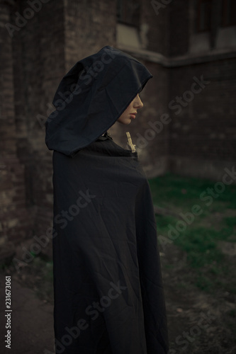 Fotografie Beautiful young nun in black cassock and hooded cloak with cross in her hands