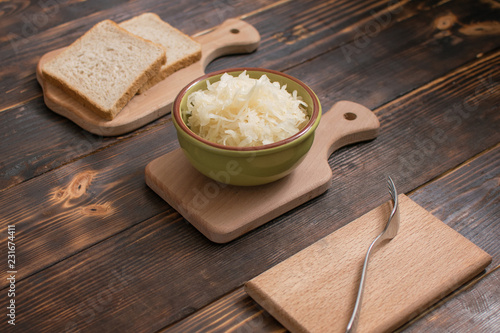 Sauerkraut in a plate and a piece of bread on a wooden background.