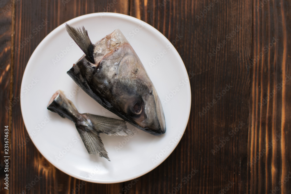 Raw head and tail of mackerel fish on a plate. The remains of butchering fish. Raw head and tail of mackerel fish on a plate. The remains of butchering fish.
