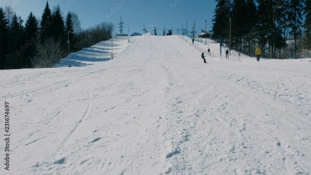 Teenage boy of 12 years in grey suit sliding on a snowboard from snow descent next sky lift. View from afar. Teenage boy of 12 years in grey suit sliding on a snowboard from snow descent next sky lift. View from afar.