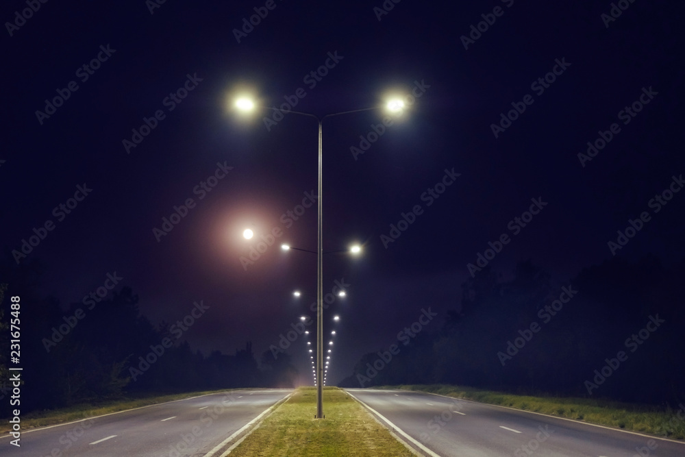 a two way road is illuminated by the light post - obrazy, fototapety, plakaty 