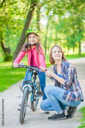 Smiling mom teaches her daughter to ride a bicycle in the park