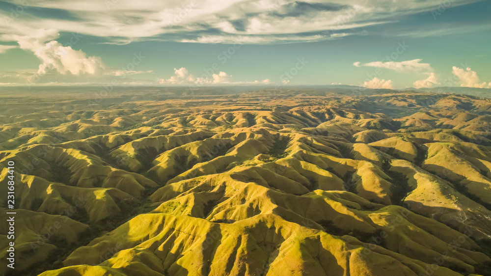 Fototapeta Aerial panorama green hills. Drone shot. Indonesia. Breathtaking landscape hilly surface on the blue cloudy sky background. Sumba island. Magnificient beauty of wild virgin nature.