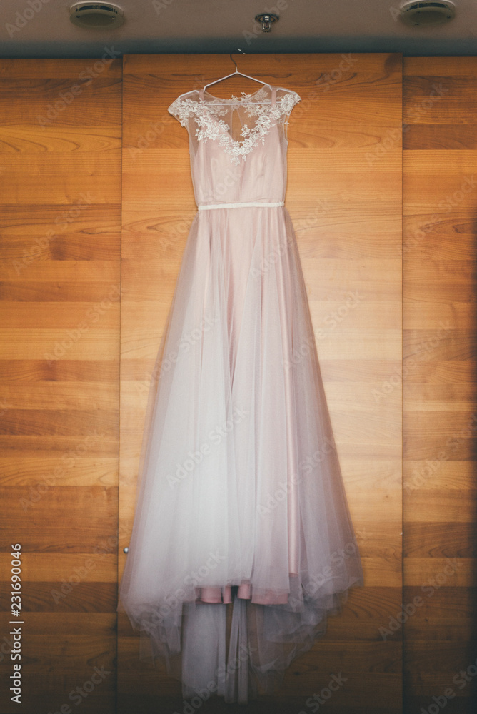 Close up of wedding dress in pastel rose hangs, wooden background Close up of wedding dress in pastel rose hangs, wooden background