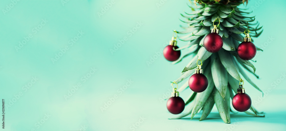 Creative Christmas tree made of pineapple and red bauble on blue background, copy space. Greeting card, decoration for new year party. Holiday concept. Banner