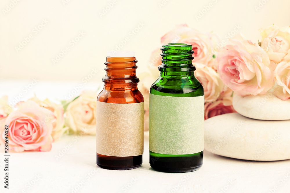 Glass bottles of essential oils on table with delicate beige rose flowers, spa stones. Aromatherapy & wellness Glass bottles of essential oils on table with delicate beige rose flowers, spa stones. Aromatherapy & wellness