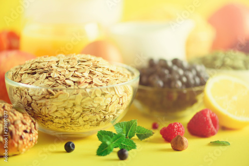 Oat flakes with milk, fresh berries, yogurt, boiled egg, nuts, fruits, orange, banana, peach for breakfast on yellow background. Copy space. Healthy food concept.