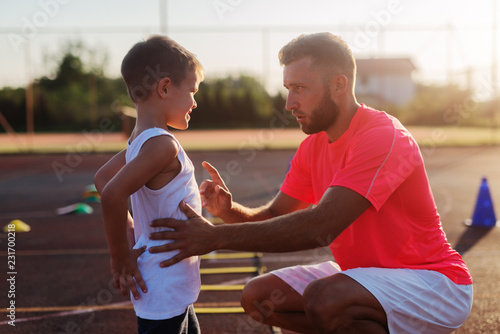 Serious young trainer giving lecture to a little boy because of his bad acting on training. photo