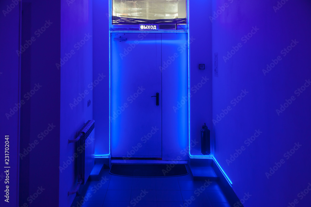 Dark corridor with a door at the end of the tunnel with blue LED illumination around the perimeter and an inscription exit at the top Dark corridor with a door at the end of the tunnel with blue LED illumination around the perimeter and an inscription exit at the top