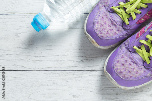 Sport flat lay purple shoes and water bottle on white wooden background with copyspace for your text. Concept healthy lifestyle and diet.