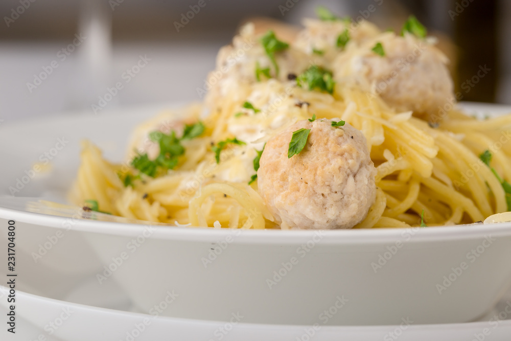 Spaghetti with creamy chicken meatballs served on white plate with pine nuts. Close up