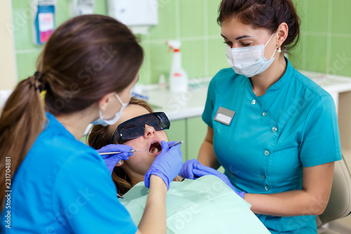 Beautiful young woman having dental treatment at dentist s office. female dentist with assistant close up