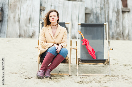 Young ginger woman with red ubrella sitting on a beach chair photo