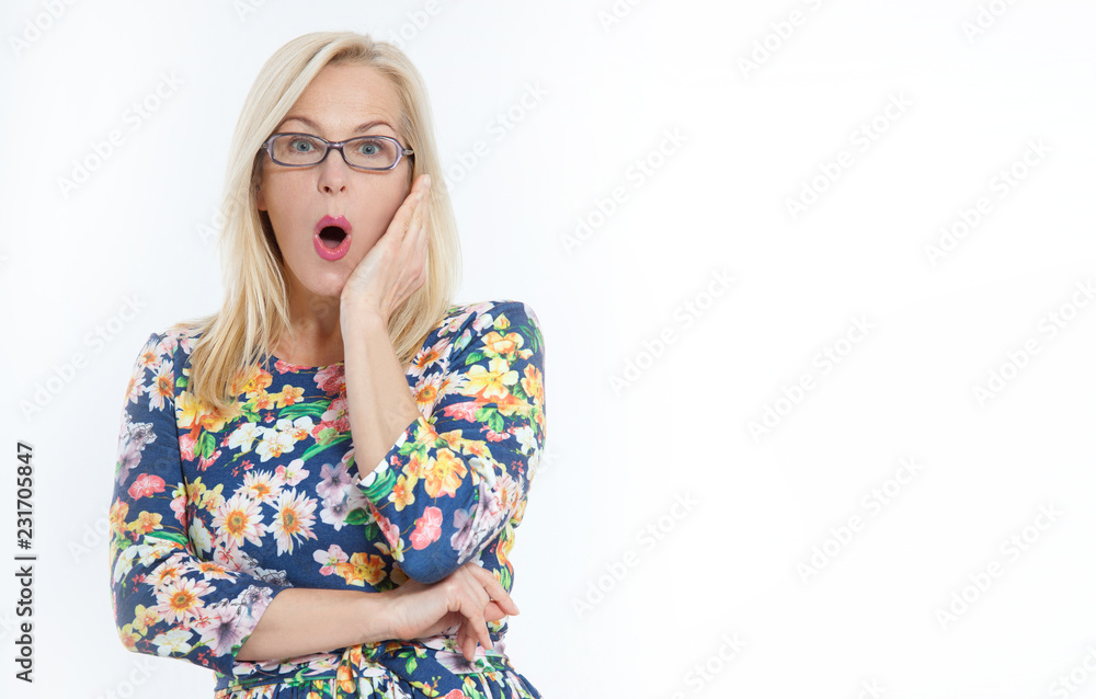 Happy Woman with glasses and surprised shouts holds cheeks by hand. Beautiful woman with blond hair pointing to look. Presenting your product. Expressive facial expressions middle-aged woman. Happy Woman with glasses and surprised shouts holds cheeks by hand. Beautiful woman with blond hair pointing to look. Presenting your product. Expressive facial expressions middle-aged woman.