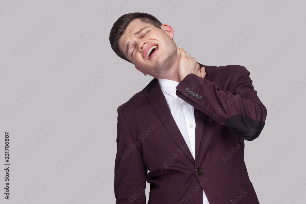 Portrait of painful sick handsome young businessman in violet suit and white shirt, standing with closed eyes and feeling pain on his neck. indoor studio shot, isolated on grey background. Portrait of painful sick handsome young businessman in violet suit and white shirt, standing with closed eyes and feeling pain on his neck. indoor studio shot, isolated on grey background.