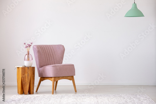 Obraz na plátně Flowers on wooden stool next to pink armchair in flat interior with copy space and mint lamp