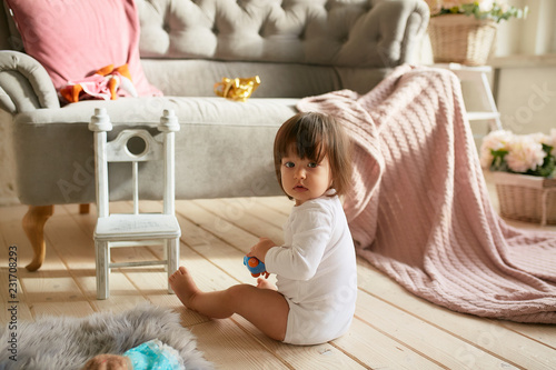 Little baby-girl in white clothes plays on the floor in a cozy pink room