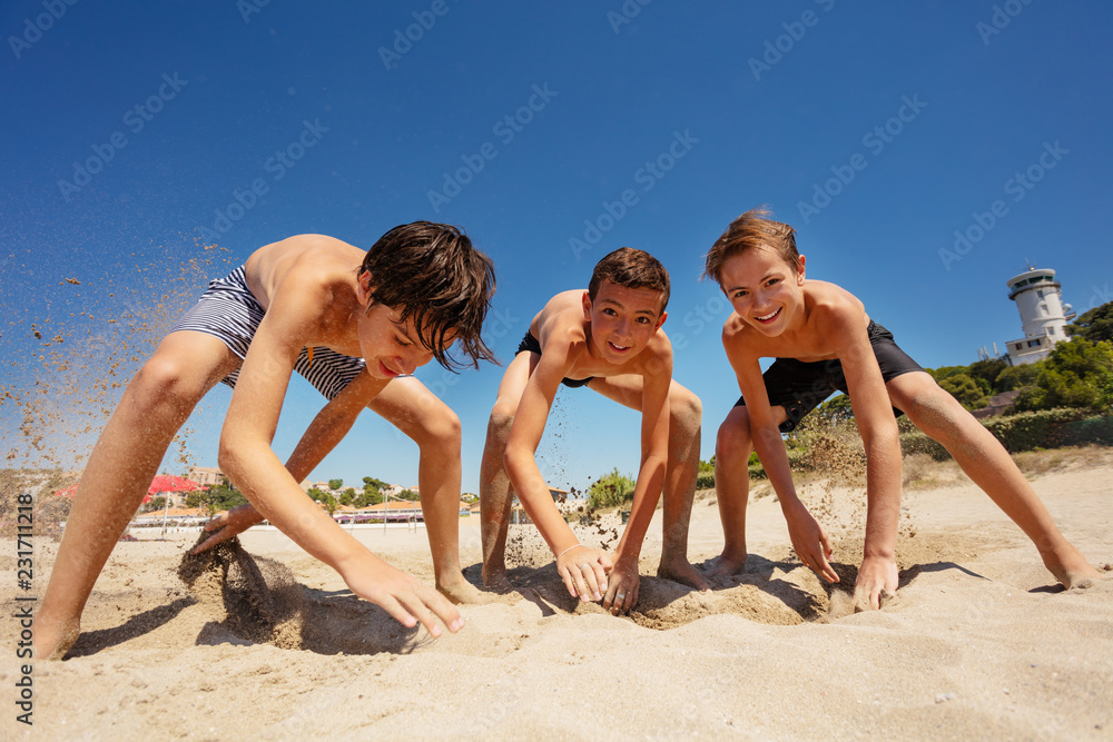 Fototapeta premium Boys digging holes with their hands on sandy beach