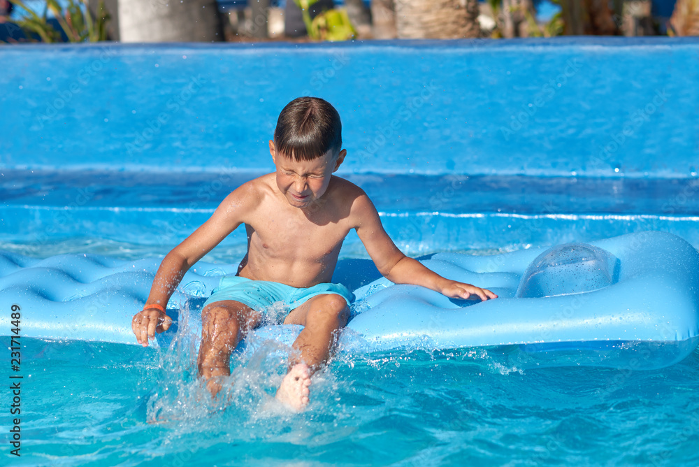 Caucasian boy sitting on inflatable mattress in swimming pool at resort. He is having fun while jumping in the pool.