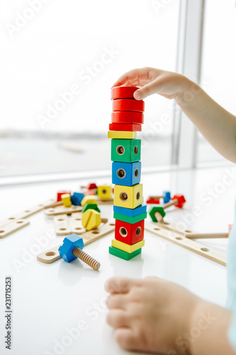 Close up of child hands playing with colorful wooden bricks at the table. Toddler having fun and building out of bright constructor bricks. Early learning