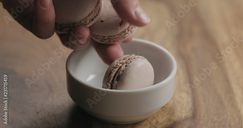 man hand put beige macarons in white bowl on wood table