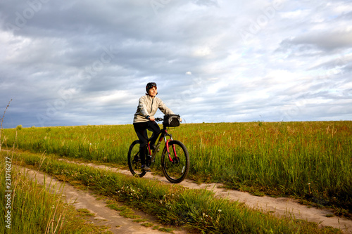 A young woman rides a bicycle on a field road. Summer sunny day