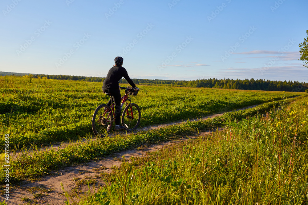 Obraz premium A young woman rides a bicycle on a field road. Summer sunny day