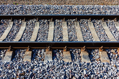 Railroad tracks with concrete sleepers. Detailed image of a railway track with gravel dumping. Side view.