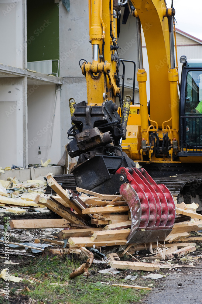 Fototapeta premium Demolition work. Excavator with grab breaking down a house.