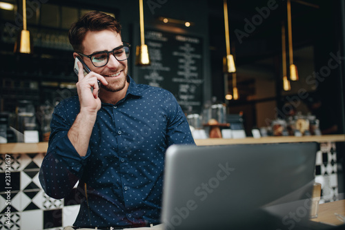 Smiling businessman talking on cell phone while working on lapto photo