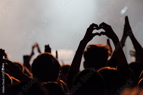 Hands silhouettes of the crowd raised up at music show. Heart made by fingers